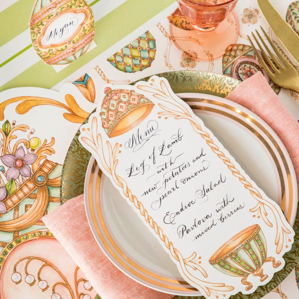 An Exquisite Egg Table Card with a menu written on it in beautiful script resting on the plate of an elegant Easter place setting.