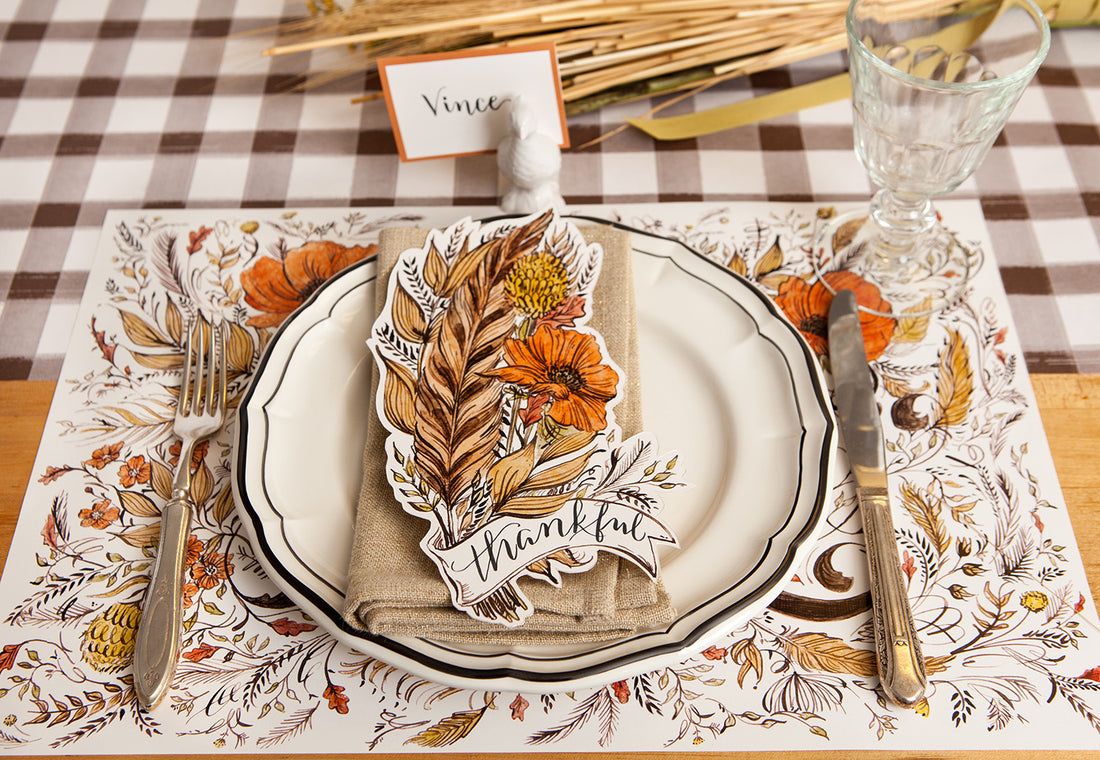 An elegant Thanksgiving place setting featuring a Feather Table Accent resting on the plate with &quot;Thankful&quot; written on it in beautiful script.