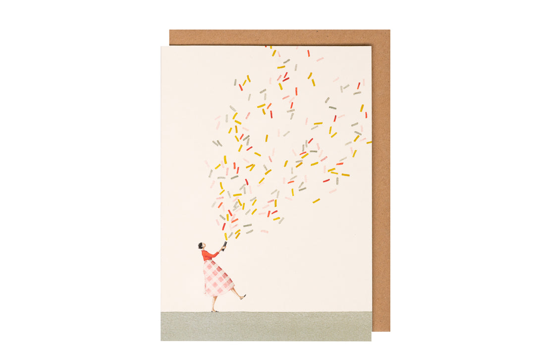 A greeting card featuring a stylized illustration of a woman shooting a confetti cannon full of multicolored confetti over the white background, with the included kraft paper envelope.