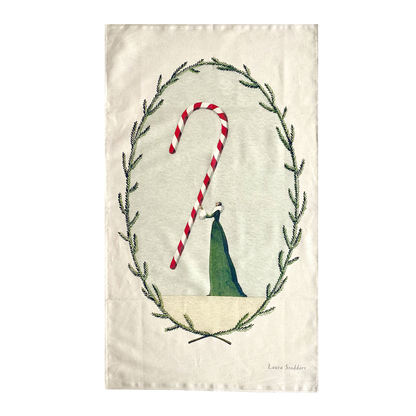 A tea towel featuring an illustration of a woman in a long green dress holding a gigantic candy cane within a frame of winter foliage.