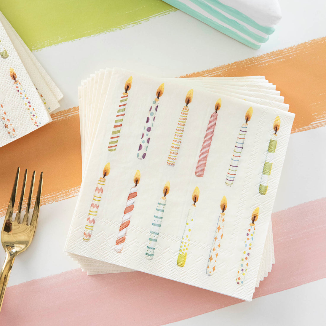 A stack of Birthday Candles Cocktail Napkins on a colorful Birthday table.