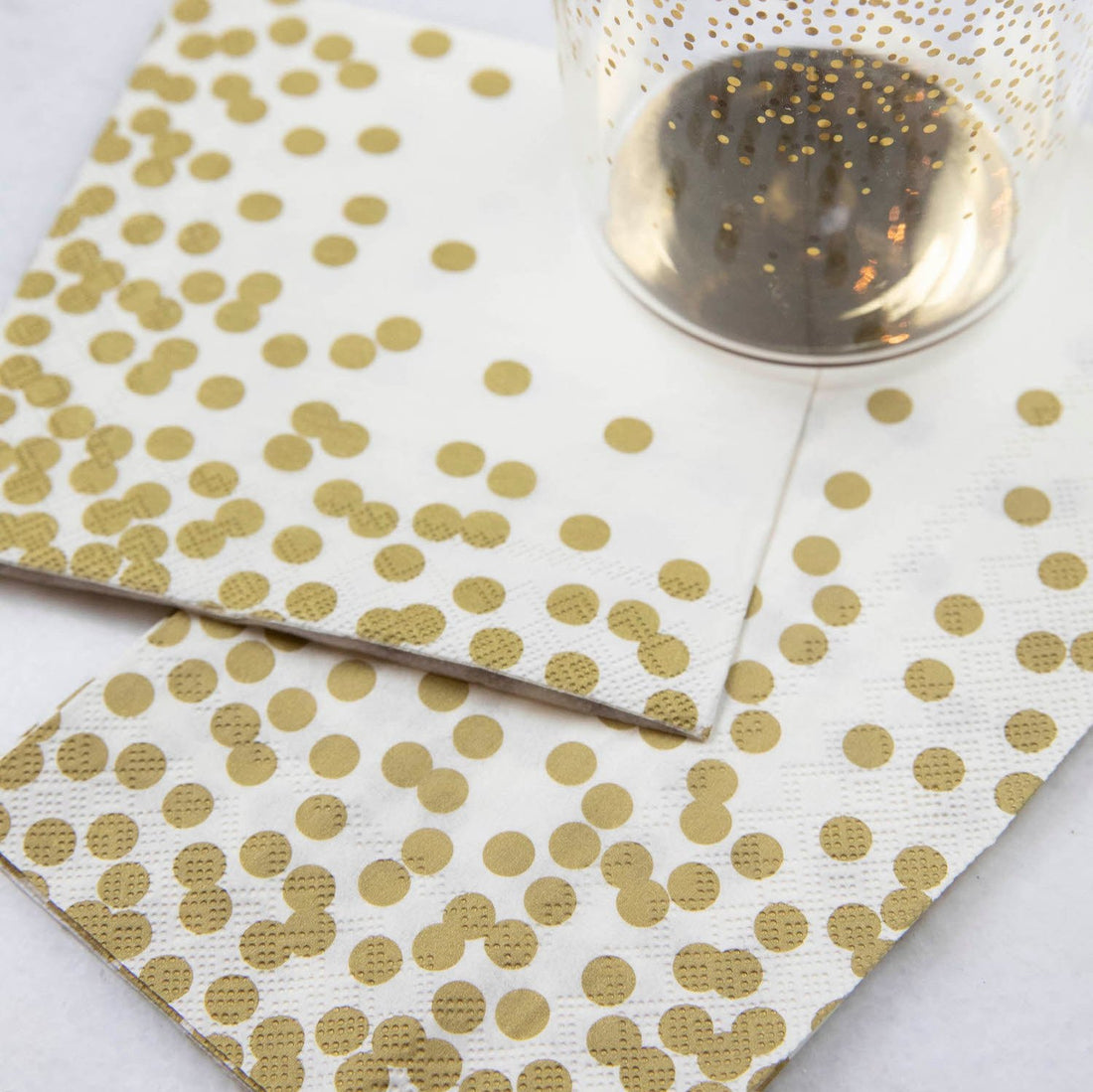 Two Gold Confetti Napkins, one Cocktail and one Guest, under a gold-accented glass on a white table.