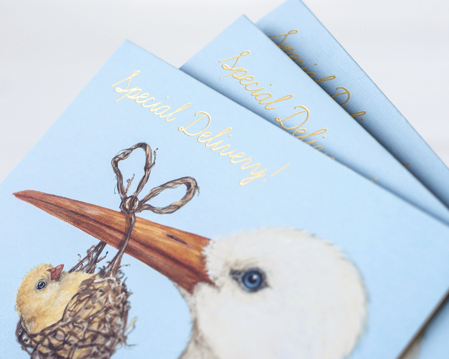 Close-up of three Baby Stork cards fanned out on a white table, showing the shiny gold foil lettering catching the light.