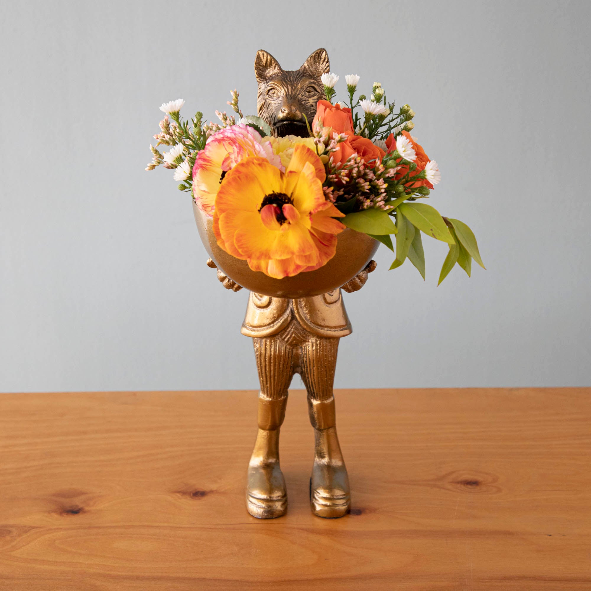 A statue of Eloise the fox holding flowers, with a brass-gold finish.