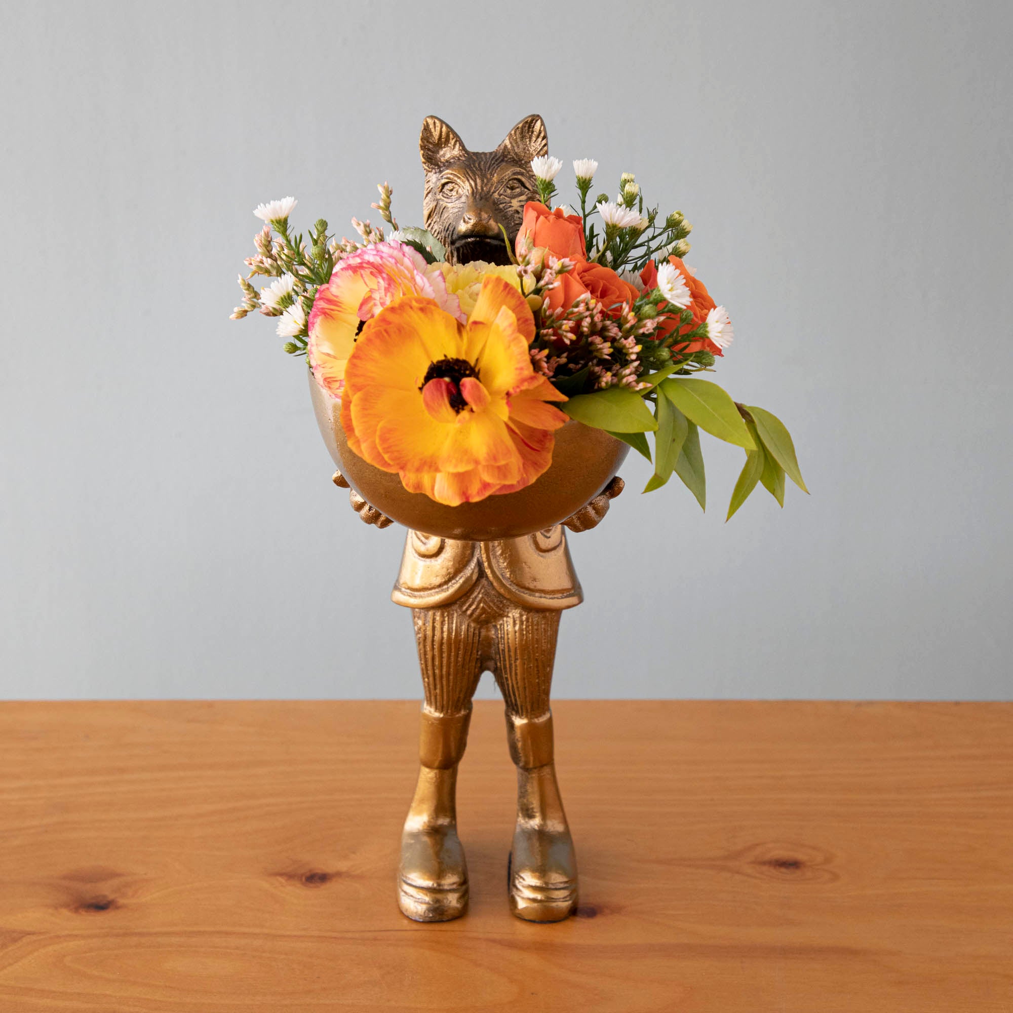 A statue of Eloise the fox holding flowers, with a brass-gold finish.