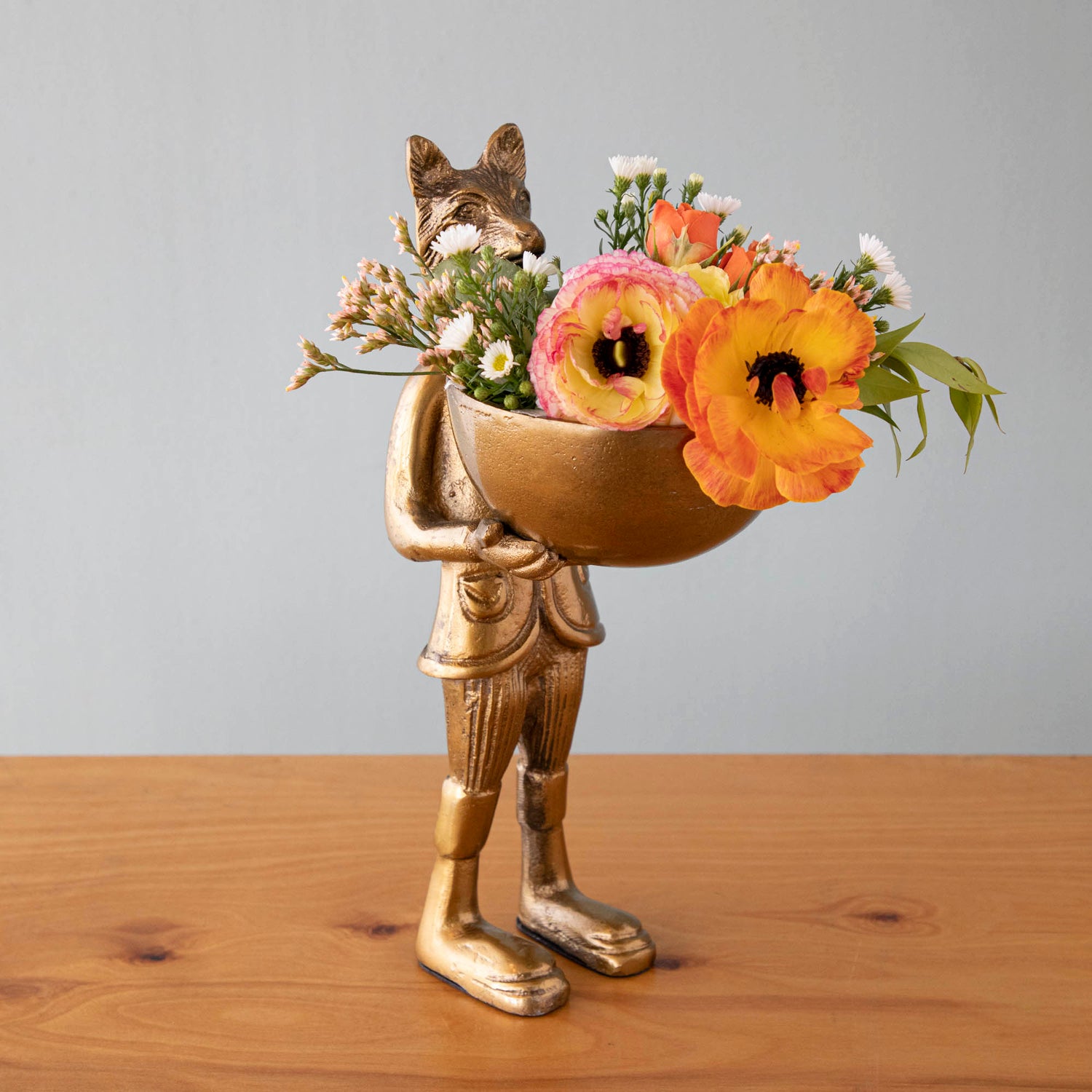 A statue of Eloise the fox holding flowers, with a brass-gold finish.