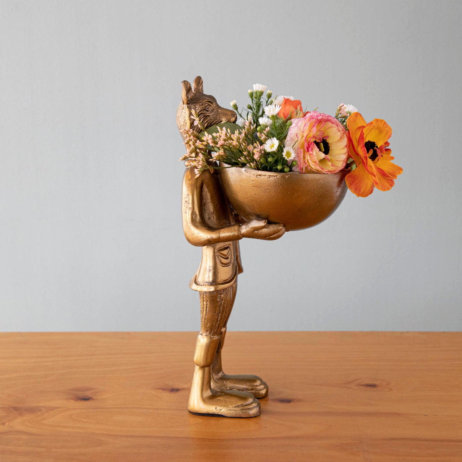 A statue of Eloise the fox holding flowers, with a brass-gold finish.