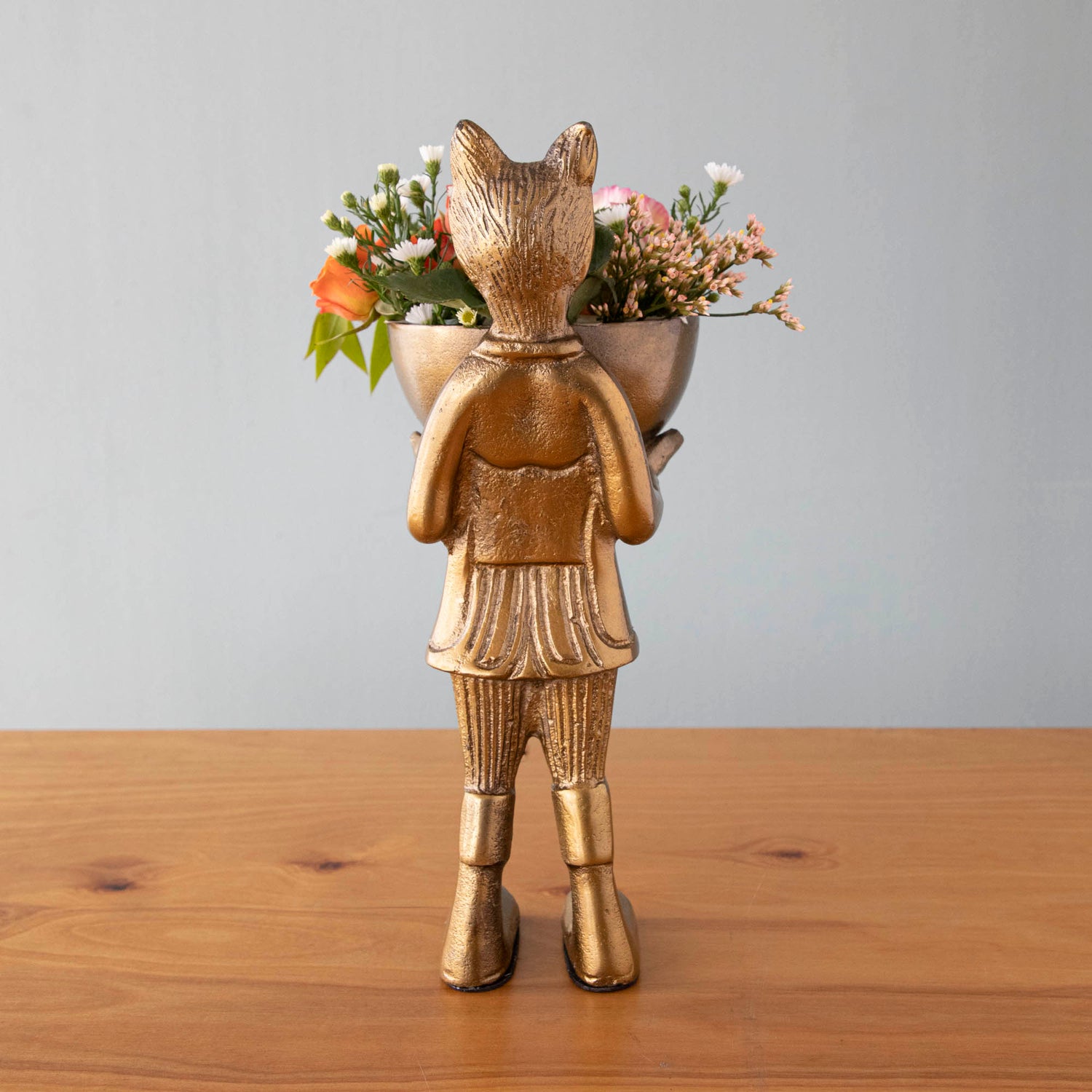 A statue of Eloise the fox holding flowers, with a brass-gold finish.