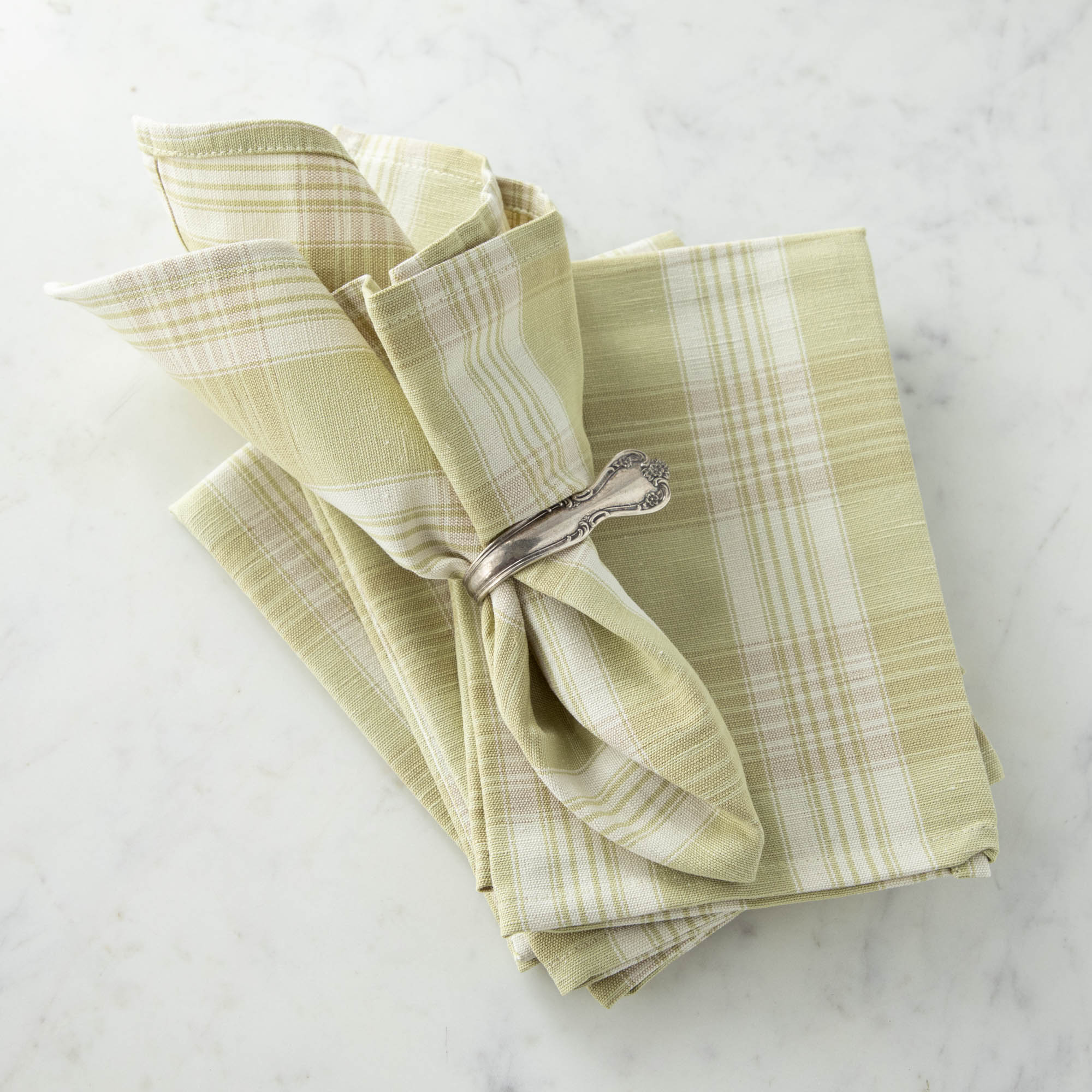 Grapefruit Plaid Napkin in a vintage silver napkin ring, on top of the same napkin, on a marble table.