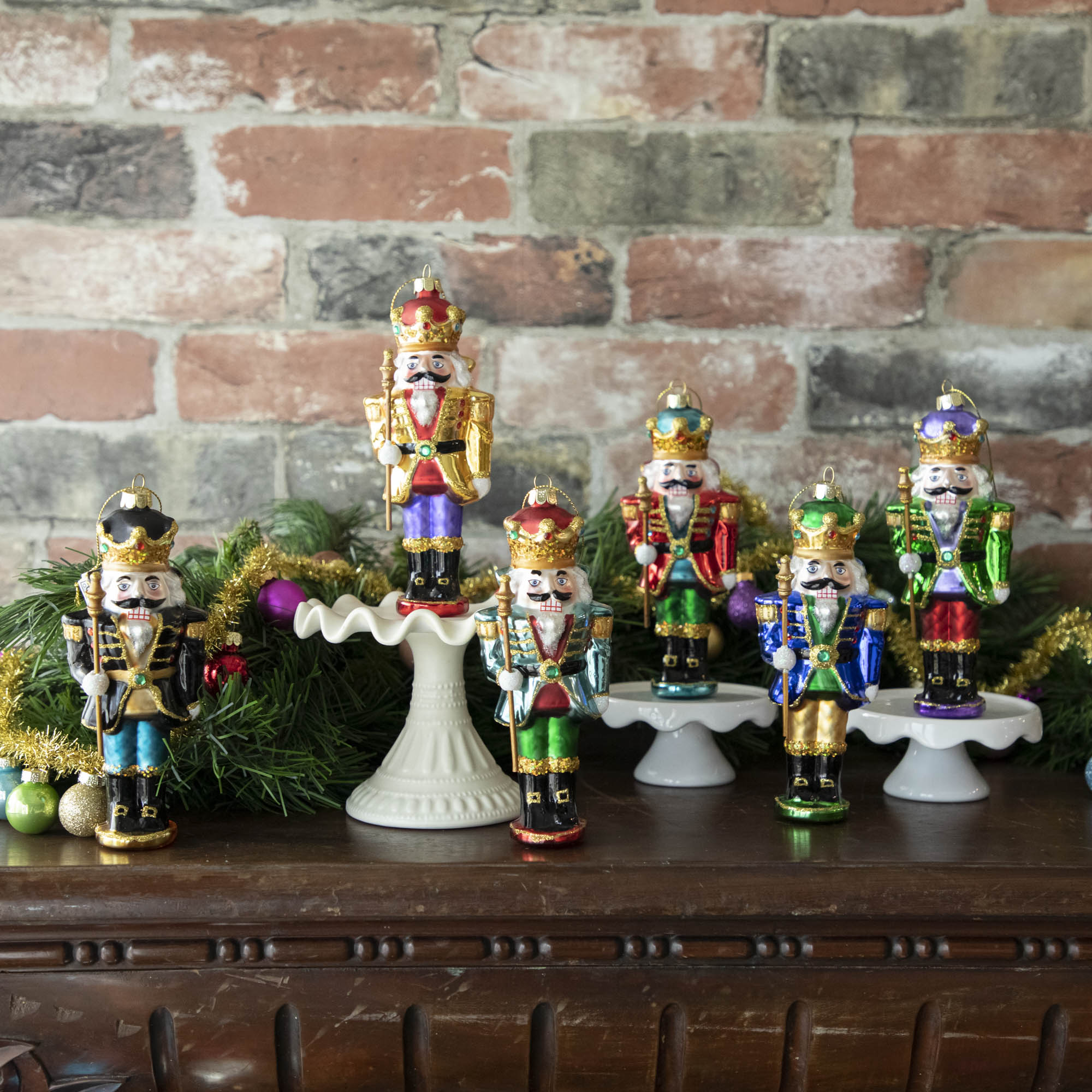 Glass Glitterville Nutcracker Ornaments on a mantle with Christmas decorations.