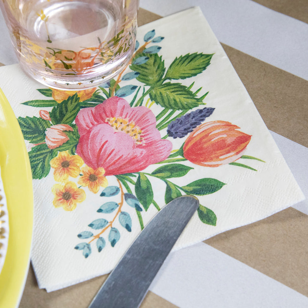 Close-up of a Sweet Garden Cocktail Napkin under a glass of water in a floral place setting.