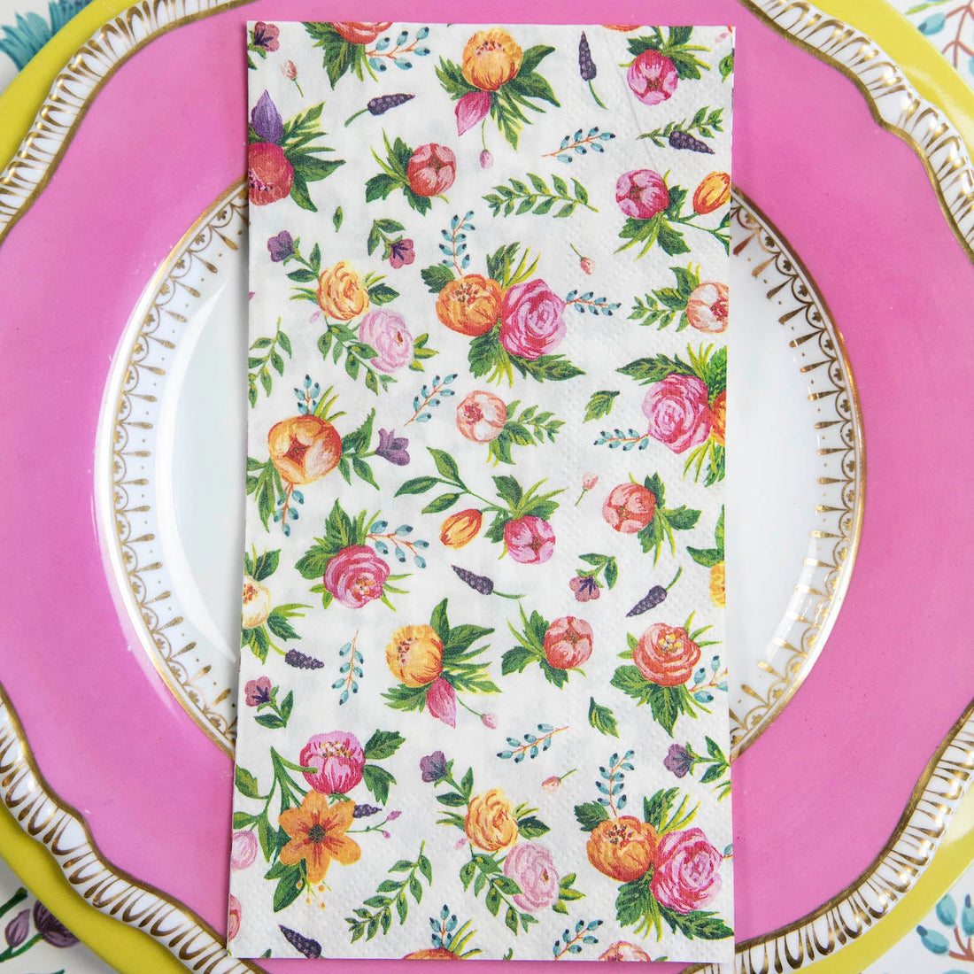 A Sweet Garden Guest Napkin centered on the pink and yellow plate in a floral place setting.