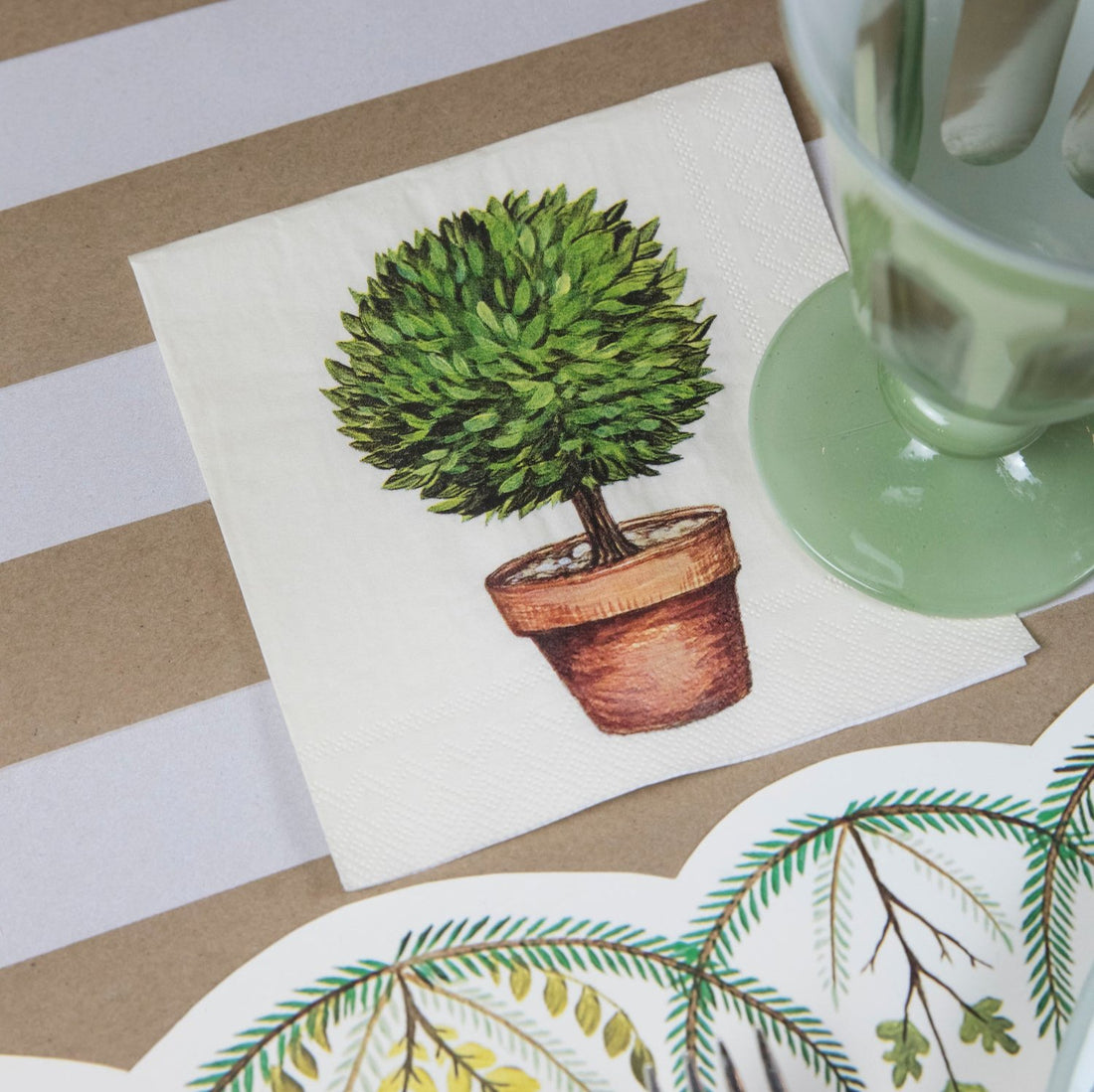 A Topiary Cocktail Napkin under a glass in a garden-themed place setting.