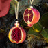 Two sliced Beaded Glass Pomegranate Ornaments hanging on a tree.