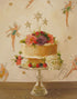 A Fairy Cake Small Art Print by Janet Hill, depicting a cake adorned with flowers and berries, encircled by illustrations of fairies and golden stars.