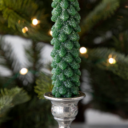 A closeup of the Green Tree Shaped Taper Candle adorned with glitter and inside of a candle holder.