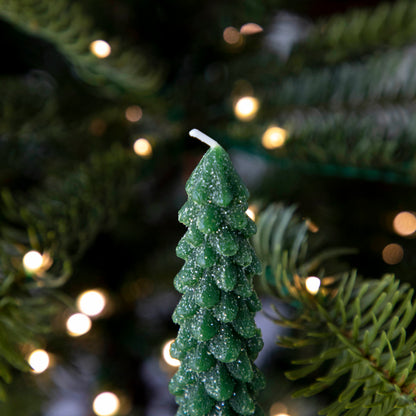 Two Glitterville Tree Shaped Taper Candles on a counter next to a Christmas tree.