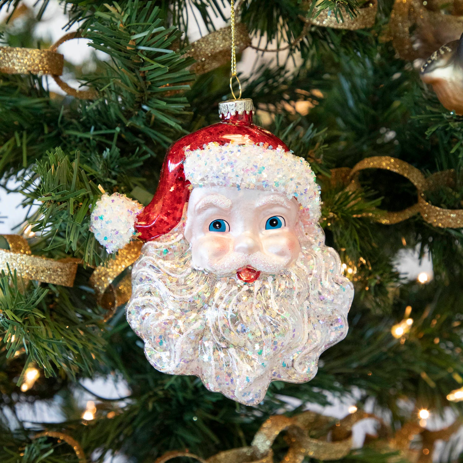 A Glitterville Glass Santa ornament, radiating festive cheer, hanging on a Christmas tree.