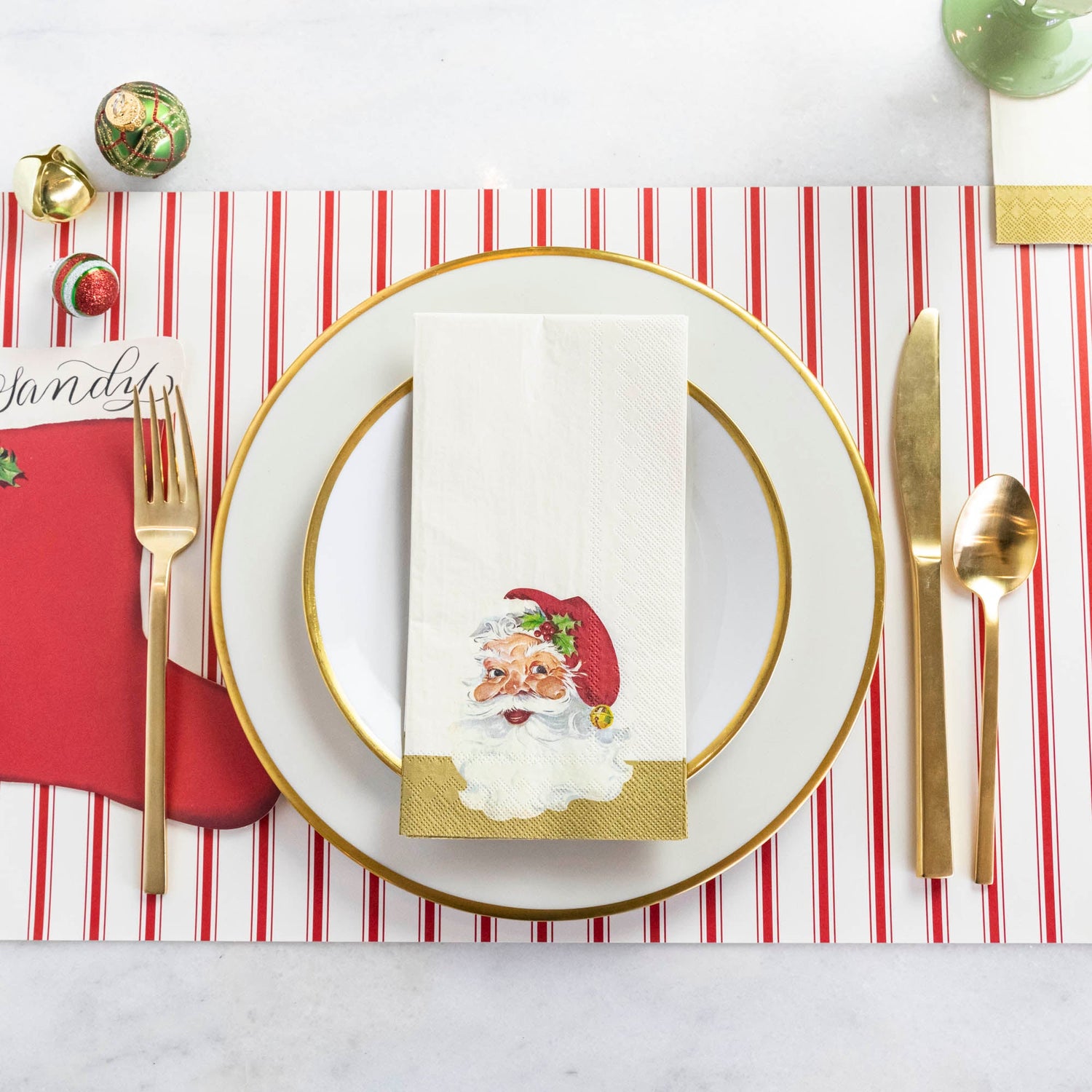 A Santa Guest Napkin centered on a plate in a Christmas place setting, from above.