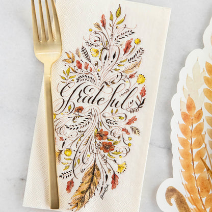 A Grateful Guest Napkin under a gold fork in an elegant Thanksgiving place setting.