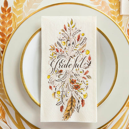 Top-down view of an elegant Thanksgiving place setting, featuring a Grateful Guest Napkin centered on a gold-rimmed plate.