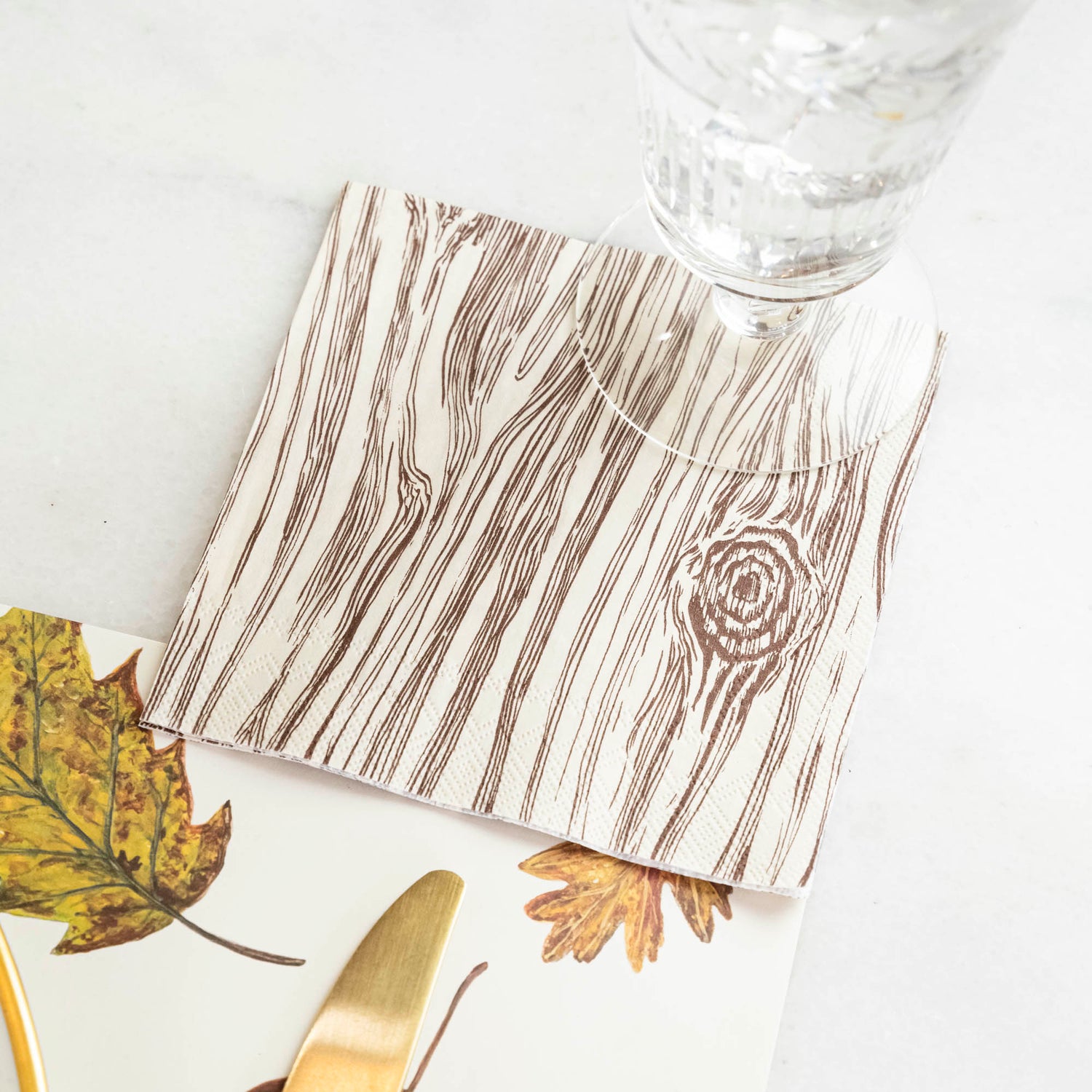 An Oak Cocktail Napkin under a water glass in a fall-themed place setting.