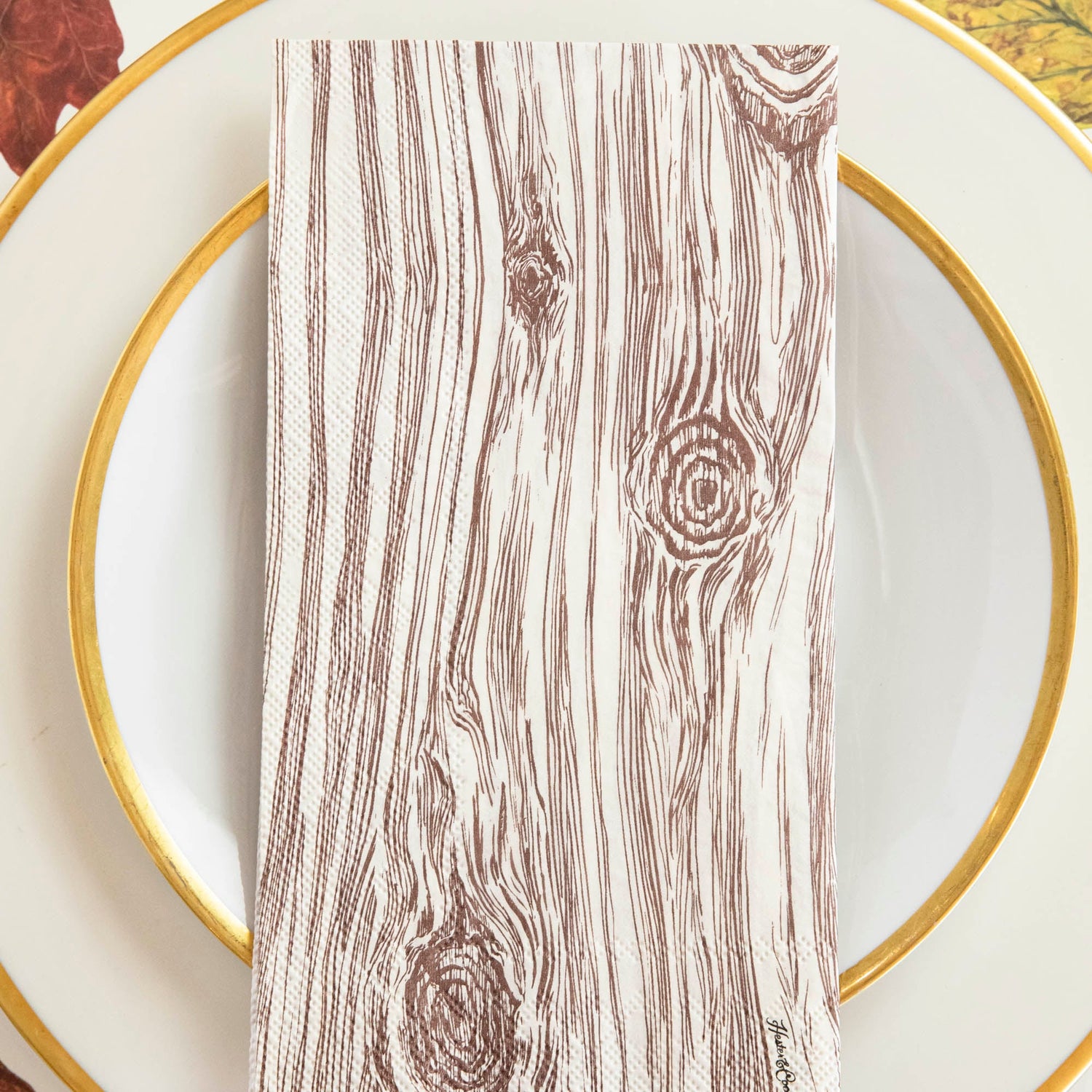An Oak Guest Napkin centered on a gold-rimmed plate in a fall-themed place setting.