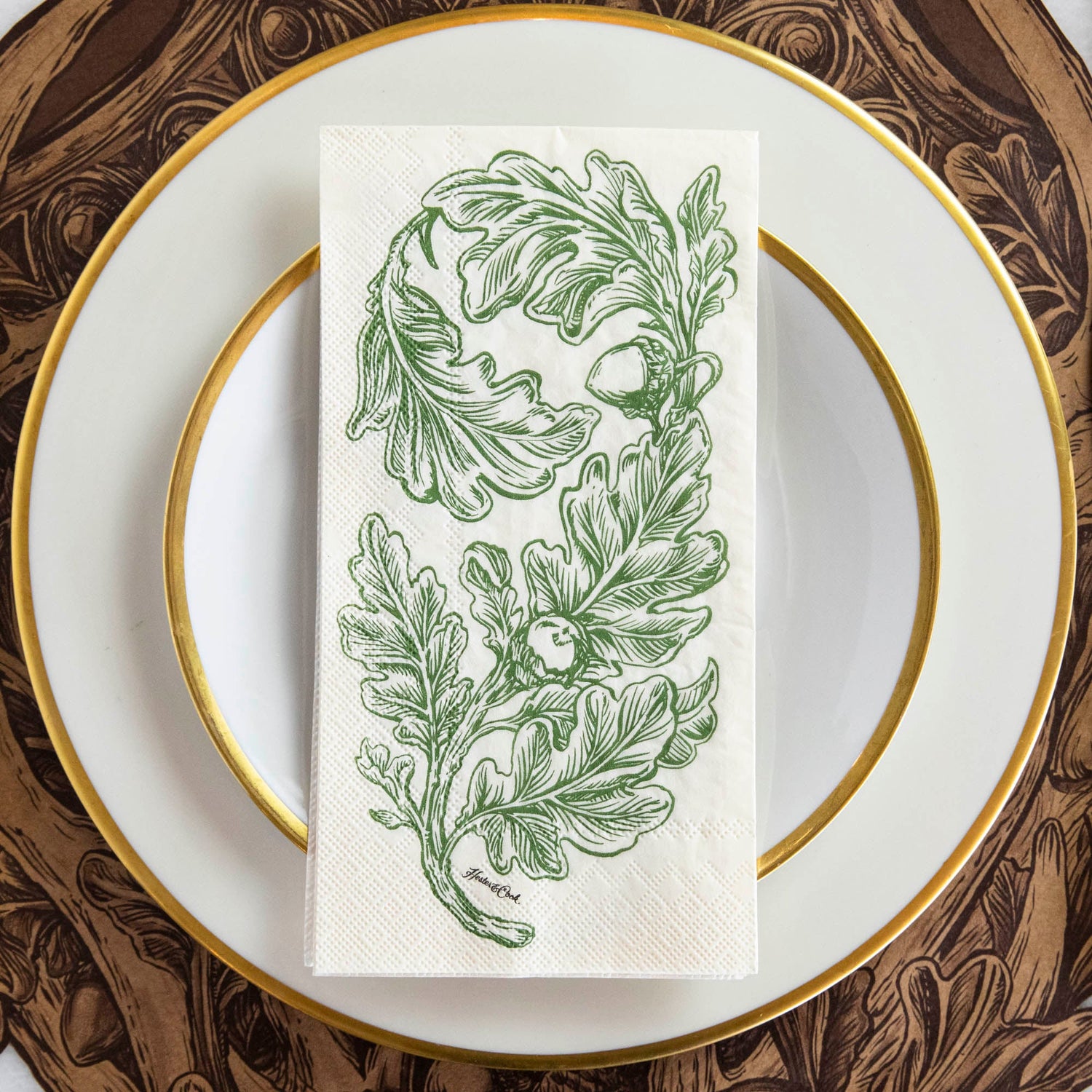 An Oak Leaves Guest Napkin centered on a gold-rimmed white plate in a rustic place setting.