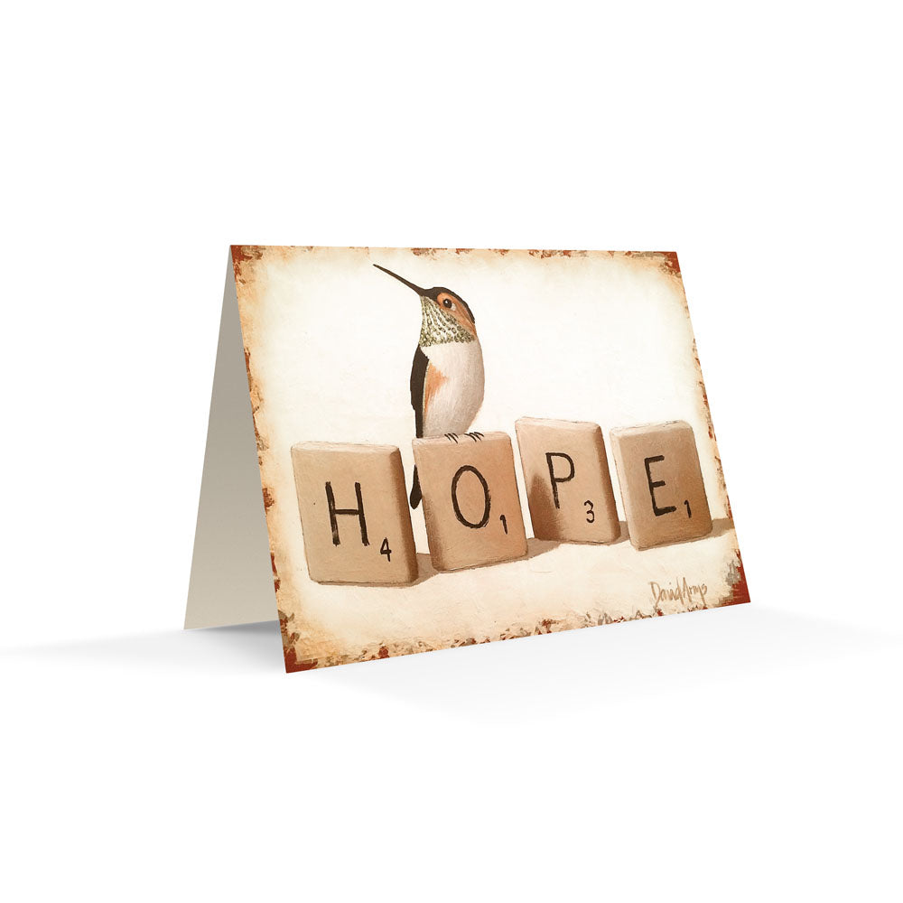 A &quot;Hope&quot; (Scrabble) notecard with a hummingbird illustration and the word &quot;hope&quot; spelled out with letter tiles rests on a woven surface. (David Arms)