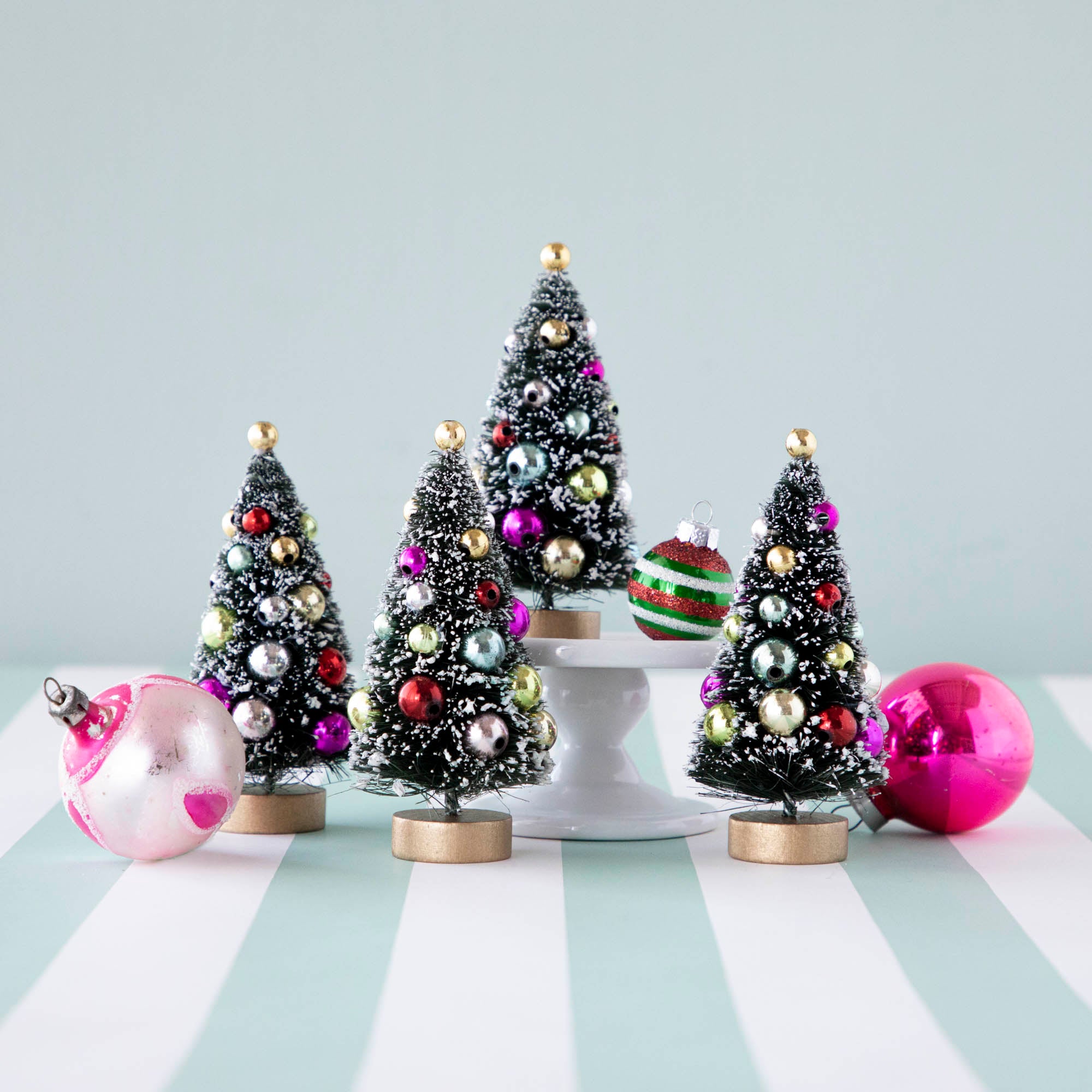 Four, 4&quot; holiday sisal trees with colorful ornaments and snow, displayed on a table with ornaments.