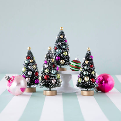 Four, 4&quot; holiday sisal trees with colorful ornaments and snow, displayed on a table with ornaments.