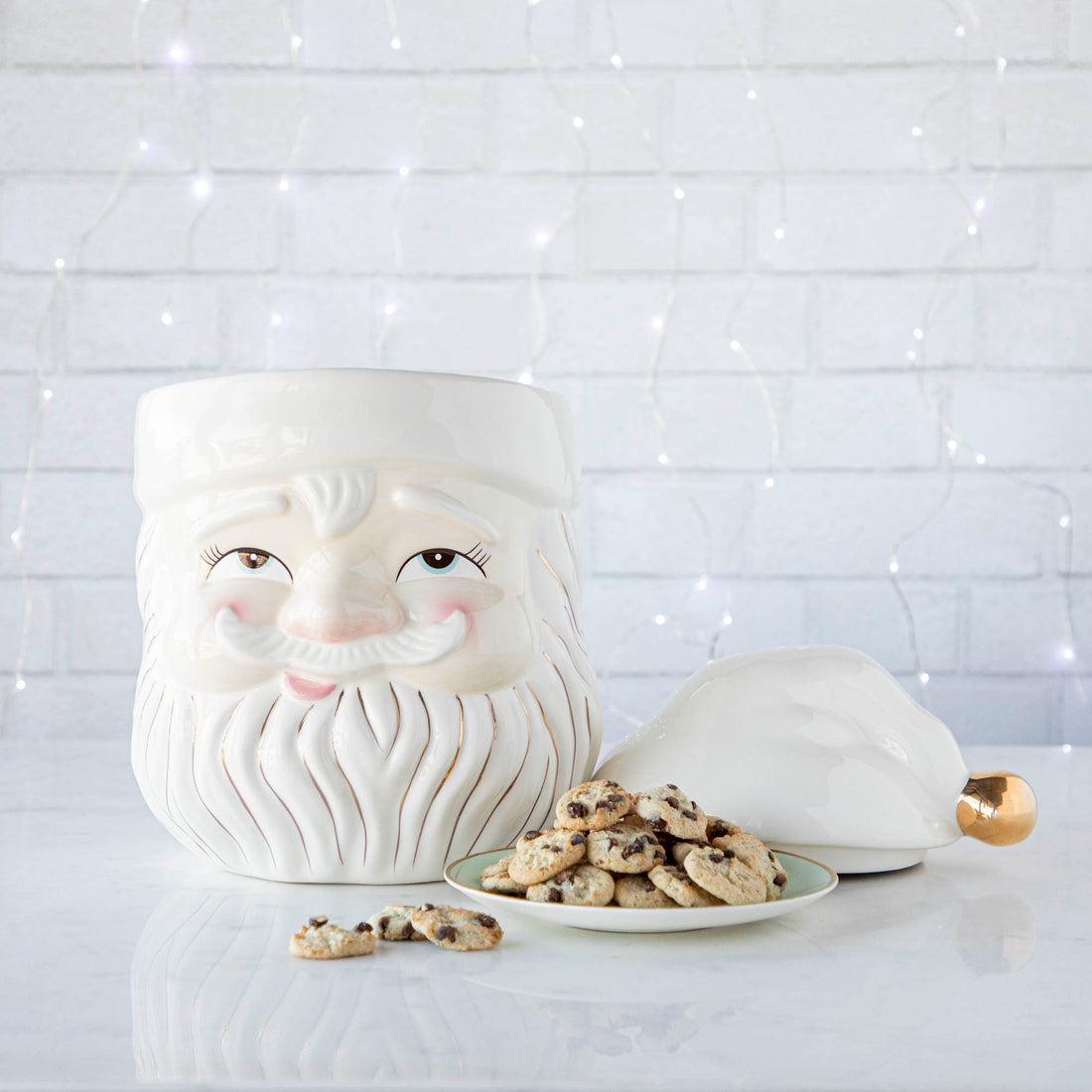 The Papa Noel Cookie Jar with the top off and a plate of cookies next to it and string of lights behind.