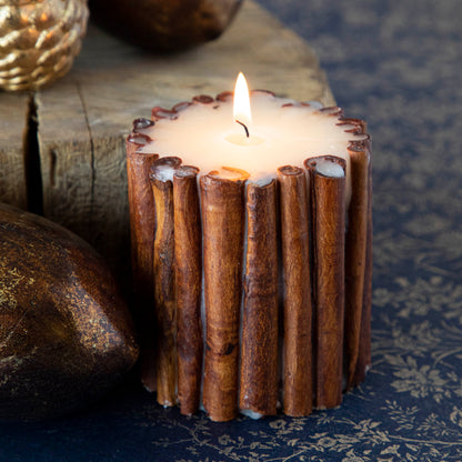 The small Cinnamon Stick Scented Pillar Candle lit, propped next to brass acorns and a tree stump.