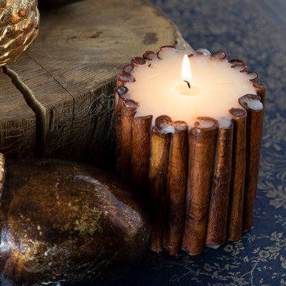 The small Cinnamon Stick Scented Pillar Candle lit, propped next to brass acorns and a tree stump.